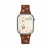 Slim vegan leather Apple Watch band with brown linen texture, featuring detailed embroidery of red cherries, pink bows, and wildflowers. Shows silver metal buckle and contrasting olive green leather loops. Perfect gift for her.