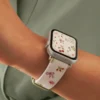Slim vegan leather Apple Watch band with white linen texture, featuring detailed embroidery of red cherries, pink bows, and wildflowers. Shows silver metal buckle and contrasting olive green leather loops. Perfect gift for her.