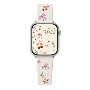 Slim vegan leather Apple Watch band with white linen texture, featuring detailed embroidery of red cherries, pink bows, and wildflowers. Shows silver metal buckle and contrasting olive green leather loops. Perfect gift for her.