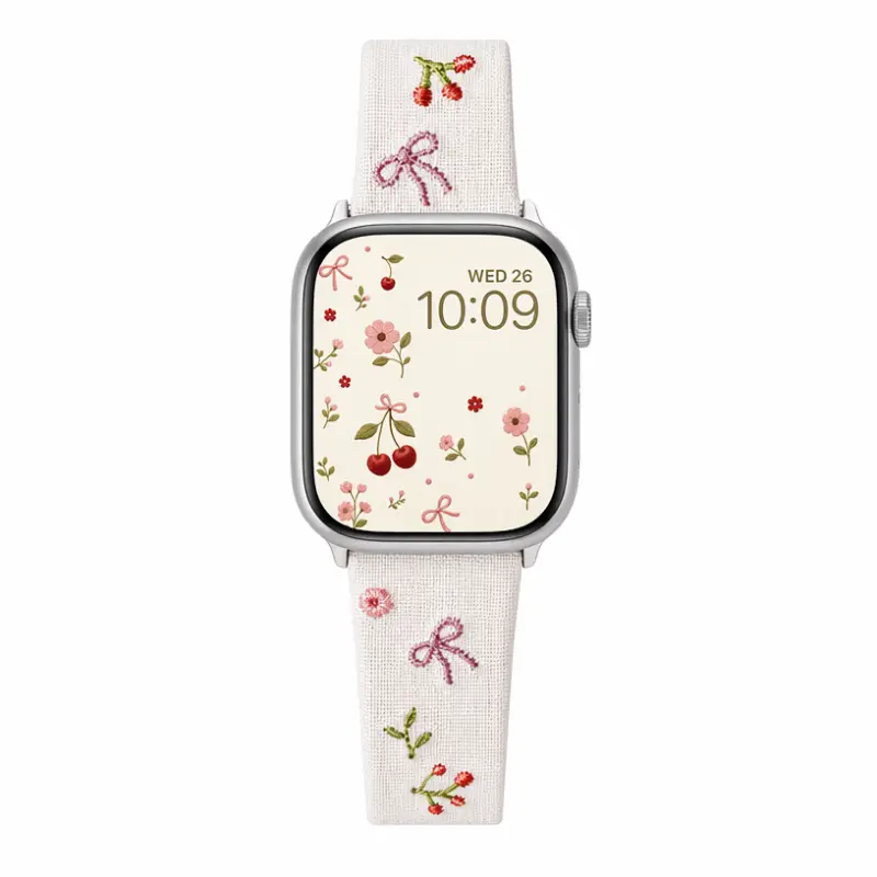 Slim vegan leather Apple Watch band with white linen texture, featuring detailed embroidery of red cherries, pink bows, and wildflowers. Shows silver metal buckle and contrasting olive green leather loops. Perfect gift for her.