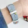 Light blue denim style vegan leather apple watch strap for women with embroidered cherries and pink bows.