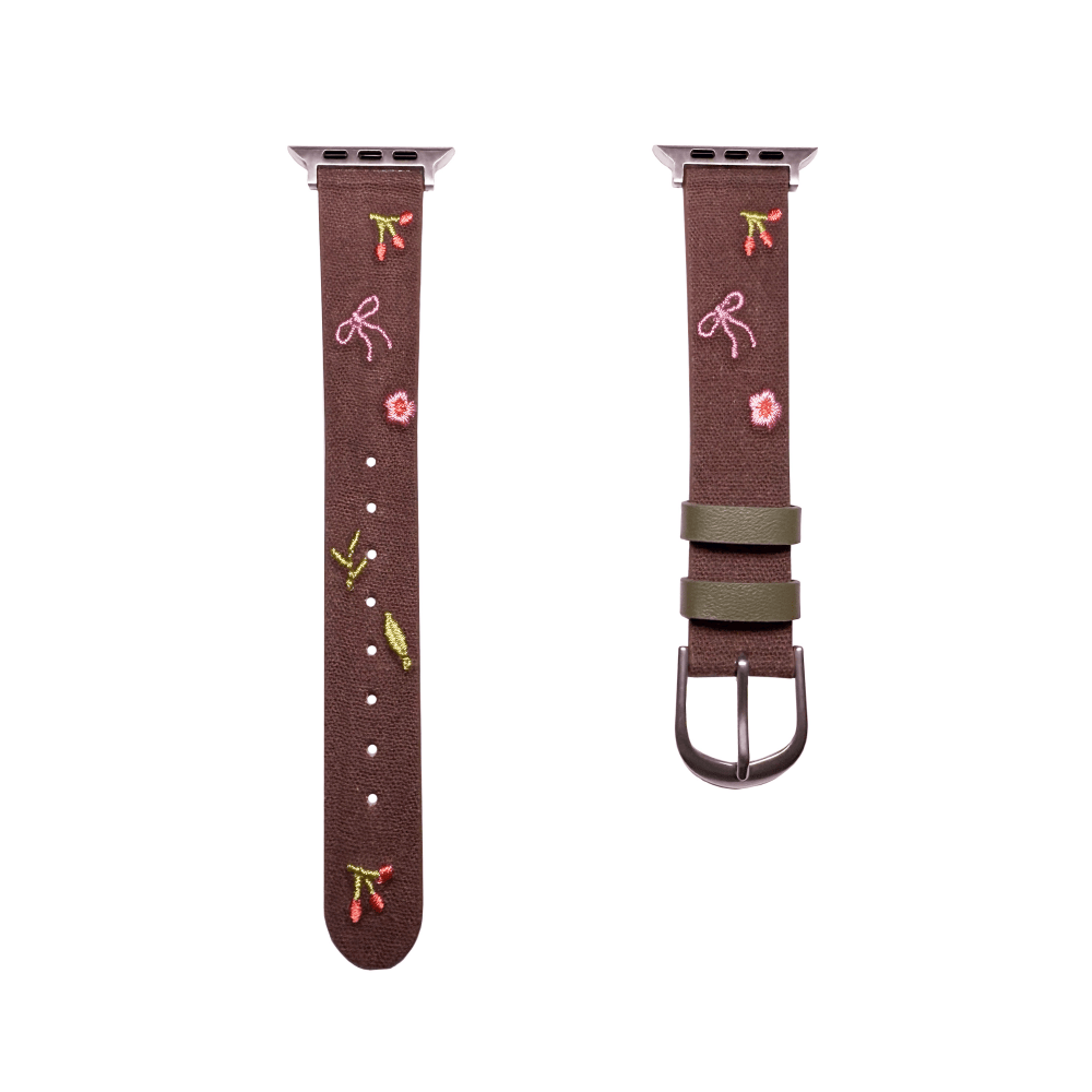 Slim vegan leather Apple Watch band with brown linen texture, featuring detailed embroidery of red cherries, pink bows, and wildflowers. Shows silver metal buckle and contrasting olive green leather loops. Perfect gift for her.