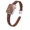 Slim vegan leather Apple Watch band with brown linen texture, featuring detailed embroidery of red cherries, pink bows, and wildflowers. Shows silver metal buckle and contrasting olive green leather loops. Perfect gift for her.