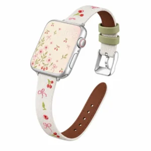 Slim vegan leather Apple Watch band with white linen texture, featuring detailed embroidery of red cherries, pink bows, and wildflowers. Shows silver metal buckle and contrasting olive green leather loops. Perfect gift for her.