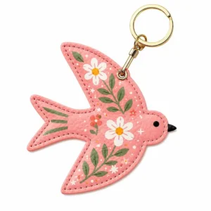 Coral pink vegan leather AirTag case shaped like a bird with white daisies and gold keyring clip.