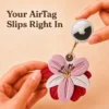 Hand holding an Apple AirTag beside a yellow vegan leather lily flower AirTag holder with gold clip
