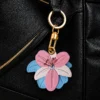 Close up of layered pink and sky blue petals with sage green leaf stitching on vegan leather AirTag case