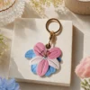 Pink and blue lily AirTag case clipped to a handbag strap, vegan leather AirTag holder for women