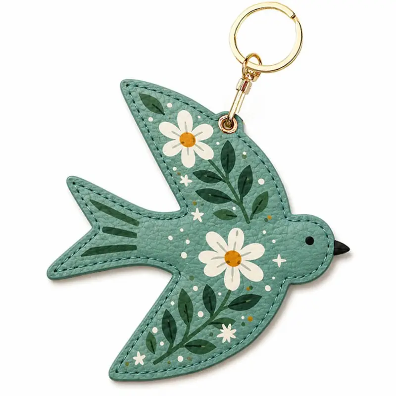 Sage green vegan leather AirTag case shaped like a bird with white daisies and gold keyring clip.