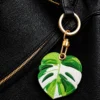 Monstera leaf vegan leather AirTag case in green and white with gold keyring clasp, cute AirTag holder for women