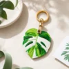 Monstera leaf vegan leather AirTag case in green and white with gold keyring clasp, cute AirTag holder for women