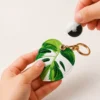 Monstera leaf vegan leather AirTag case in green and white with gold keyring clasp, cute AirTag holder for women