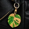 Caramel monstera leaf vegan leather AirTag case in tan and green with gold keyring, cute AirTag holder for women