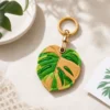 Caramel monstera leaf vegan leather AirTag case in tan and green with gold keyring, cute AirTag holder for women